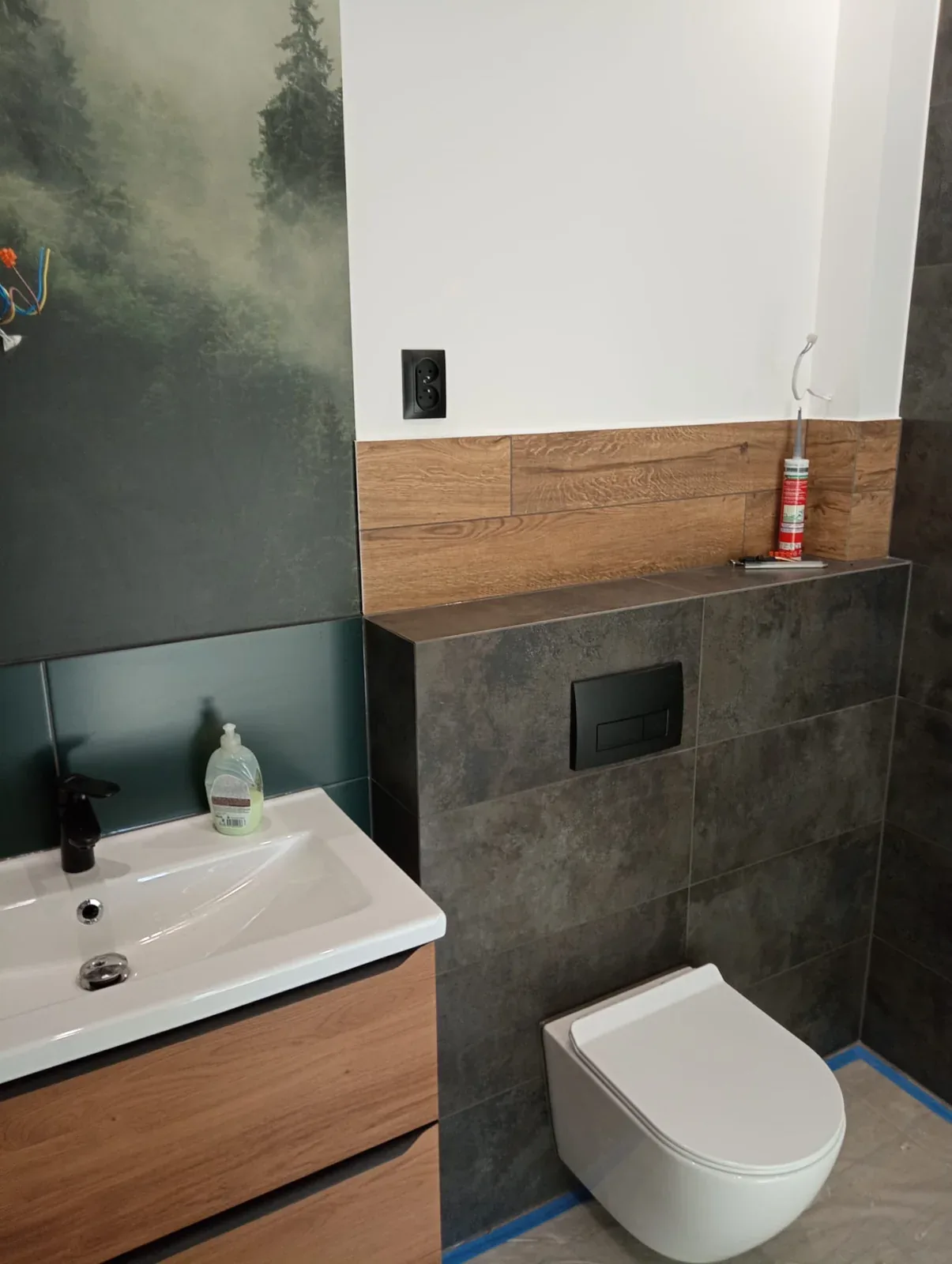 Podwieszana toaleta, zabudowa stelaża WC i drewnopodobne płytki w łazience z motywem lasu